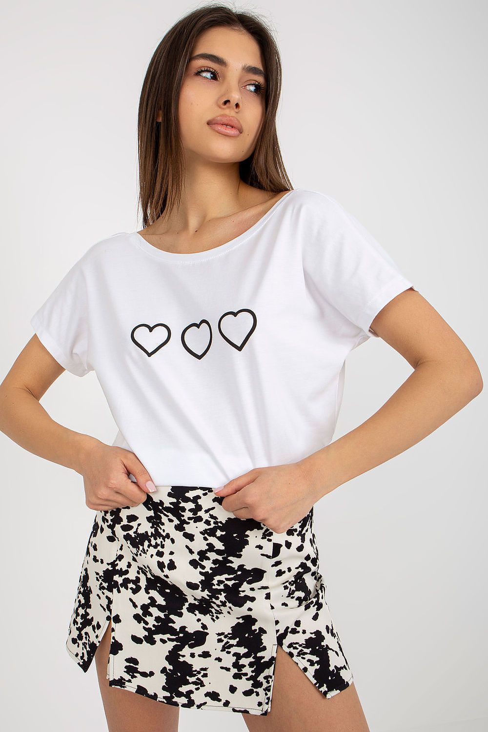 Elegant women's straight cut t-shirt by Rue Paris featuring a boat neckline and decorative heart print, styled with a chic black and white patterned skirt.