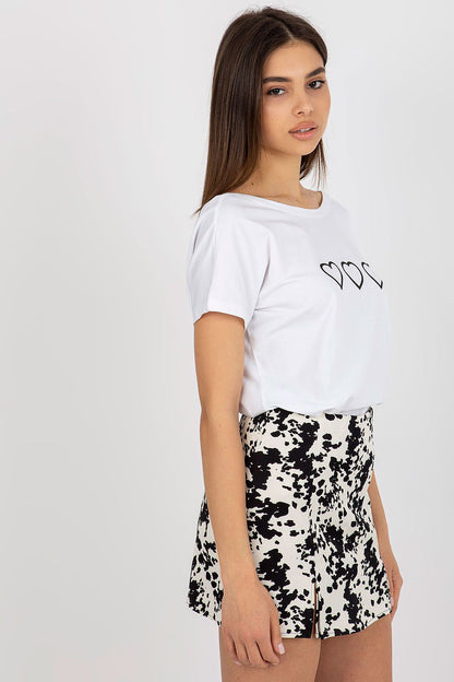 Refined women's t-shirt by Rue Paris, featuring a boat neckline and unique heart embellishments, worn with a trendy black and white patterned skirt for an elegant look.