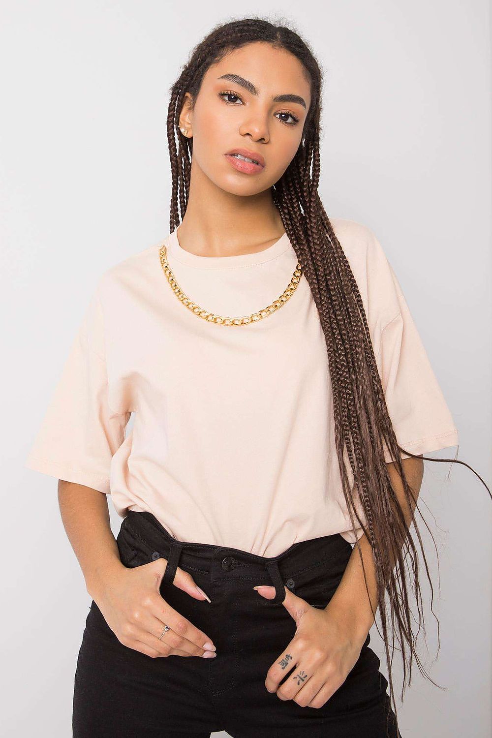 Luxurious loose fit women's t-shirt by Rue Paris, featuring a decorative chain detail, styled with black trousers and long braided hair against a simple background.