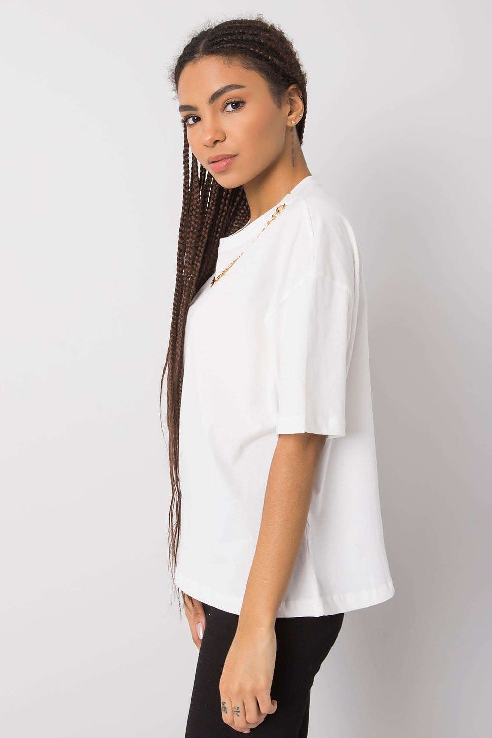 Luxurious women's loose fit white t-shirt by Rue Paris, featuring decorative chain detail, styled with braided hair and a confident look.