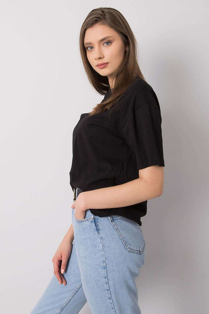 Side view of a sophisticated black loose fit t-shirt by Rue Paris, showcasing the decorative chain accent, with the model confidently posing in selected denim.