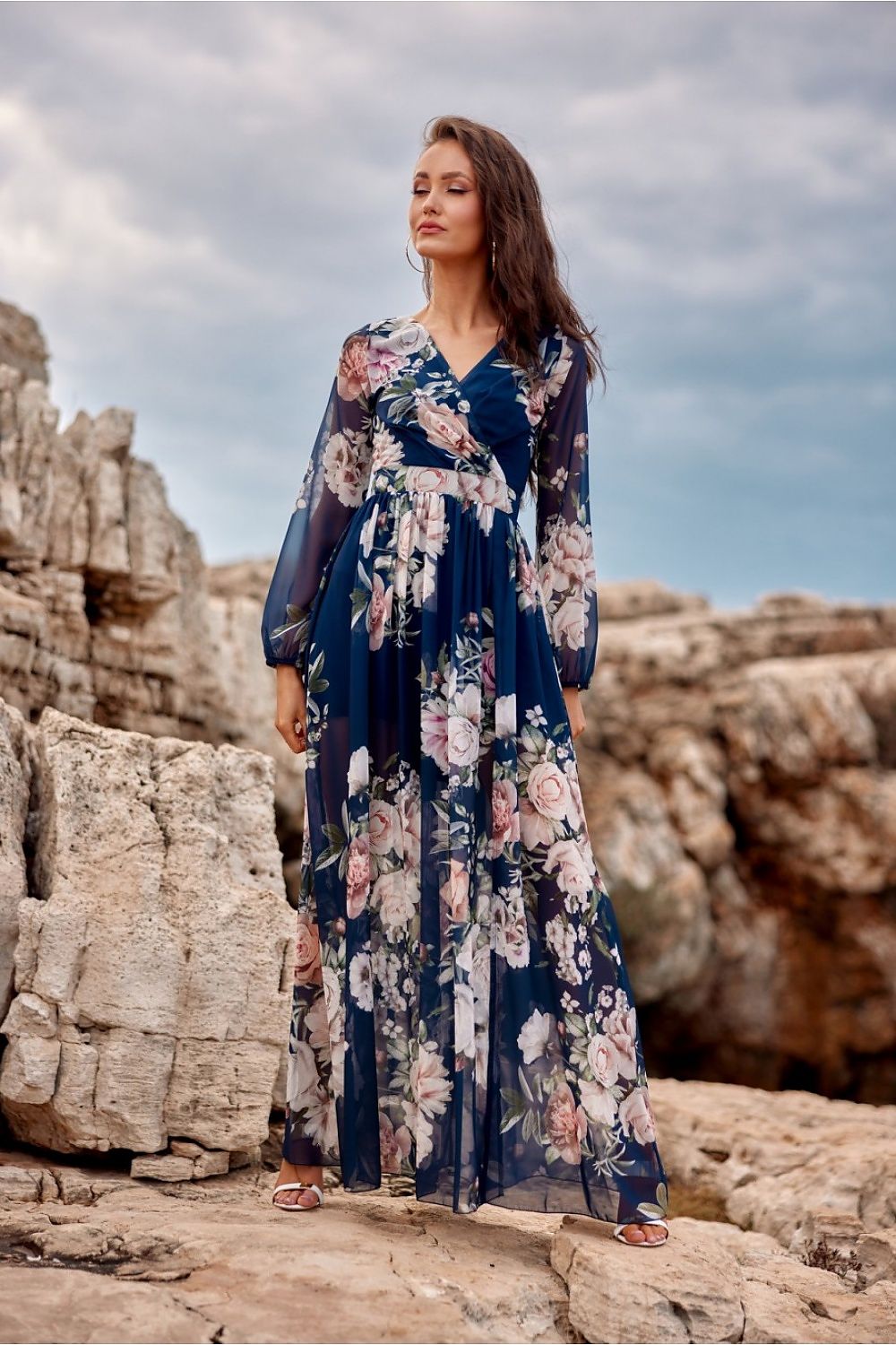 Elegant woman in a navy floral maxi dress by Roco Fashion, showcasing stylish long sleeves and a back cutout, perfect for making a statement at any evening occasion.
