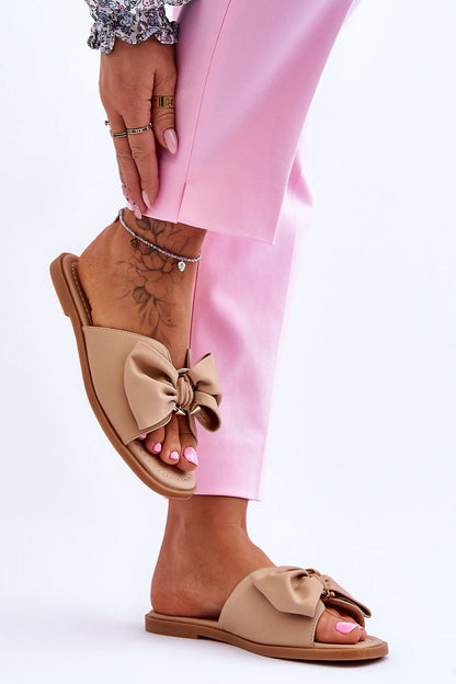 Luxurious eco-leather flip-flops in a neutral shade with a stylish bow, worn by a woman in vibrant pink trousers, by Step in Style.