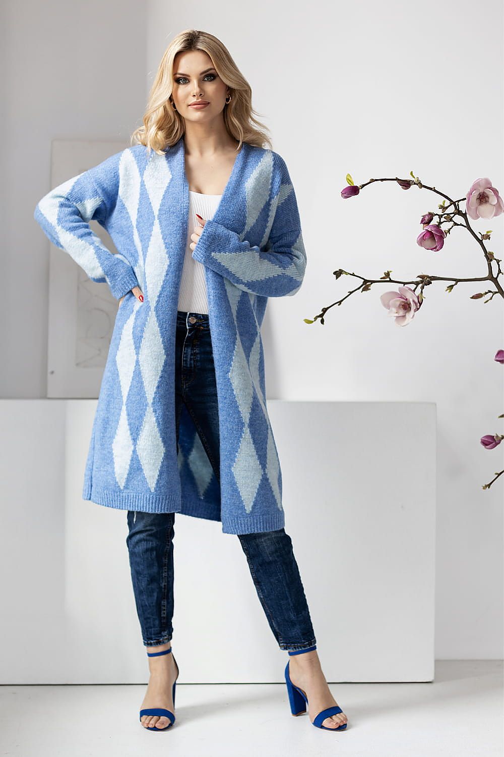 PeeKaBoo designer cardigan in blue hues with a geometric pattern, worn over a white top and denim, showcasing a luxurious style.