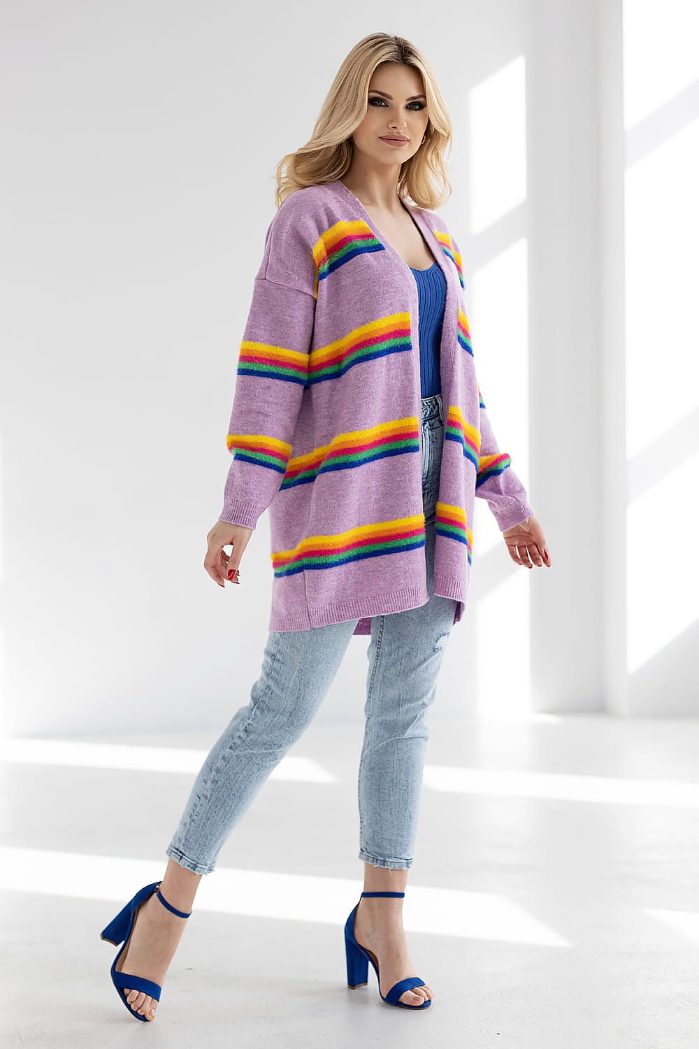 Elegant model showcasing a luxurious striped cardigan by PeeKaBoo in vibrant purples and yellows, paired with denim jeans and stylish blue heels, in a bright studio setting.