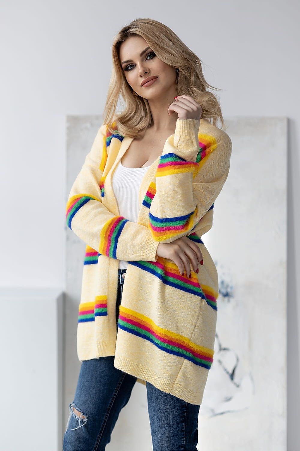 Sophisticated model dressed in a luxurious yellow striped cardigan by PeeKaBoo, exuding elegance with a natural beauty pose and paired with distressed denim.