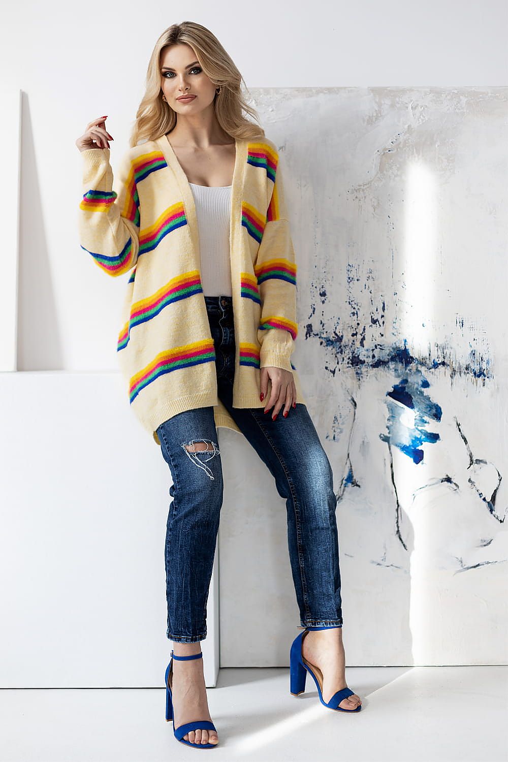 Refined shot of a model in a luxurious yellow striped cardigan by PeeKaBoo, accentuating chic fashion trends with a casual white top and stylish blue heels.
