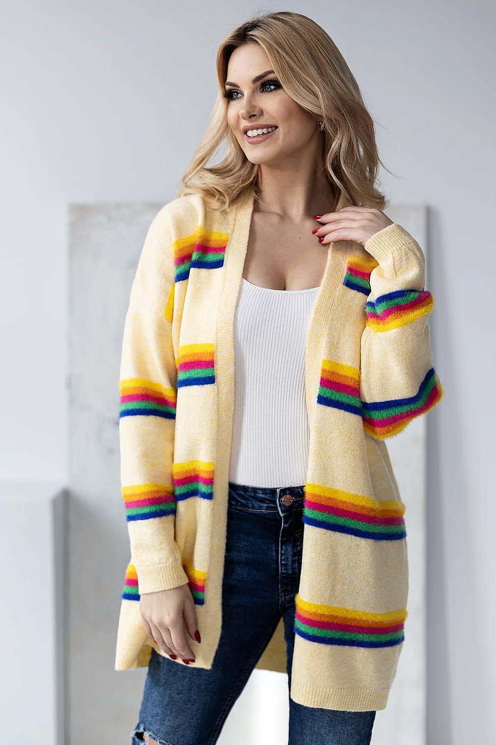 Glamorous model smiling in a luxurious yellow striped cardigan by PeeKaBoo, complemented with trendy blue denim and capturing an aura of elegance against a minimalist background.