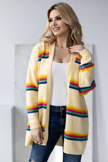 Glamorous model smiling in a luxurious yellow striped cardigan by PeeKaBoo, complemented with trendy blue denim and capturing an aura of elegance against a minimalist background.