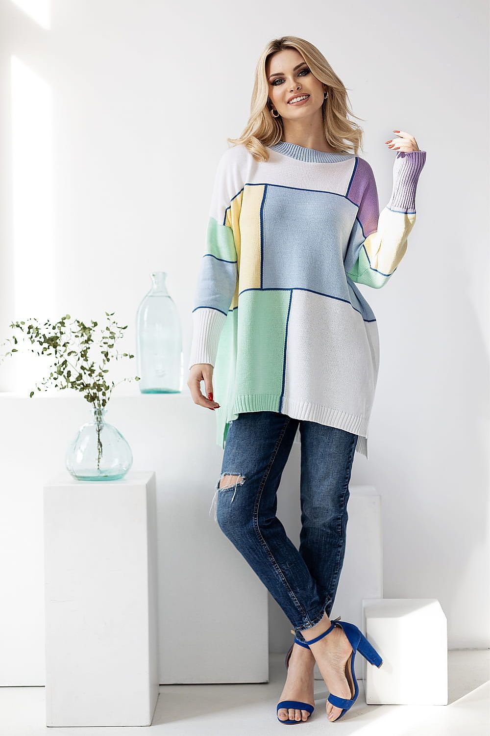 Elegant colour block sweater by PeeKaBoo, styled with a contemporary aesthetic. The model stands confidently, highlighting the luxurious fabric and relaxed fit, paired with distressed jeans and vibrant heels, set in a refined, light-filled environment.