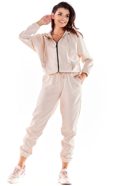 Elegant Awama loose fit tracksuit trousers in soft beige, showcasing a chic elastic waistband and sporty accents, paired with trendy sneakers.