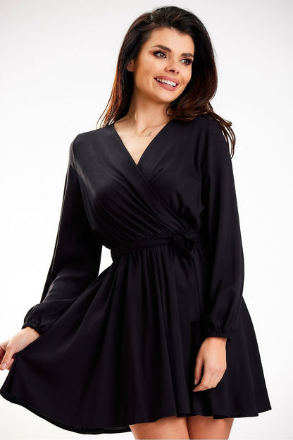 Chic black mini dress designed by Awama, highlighting long sleeves and a flattering wrap design, worn by a smiling model.