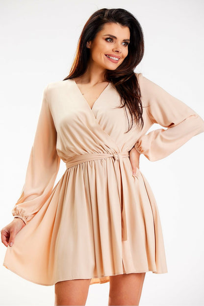 Delicate nude mini dress from Awama with a wrap design and long sleeves, elegantly worn by a smiling model, perfect for versatile styling.
