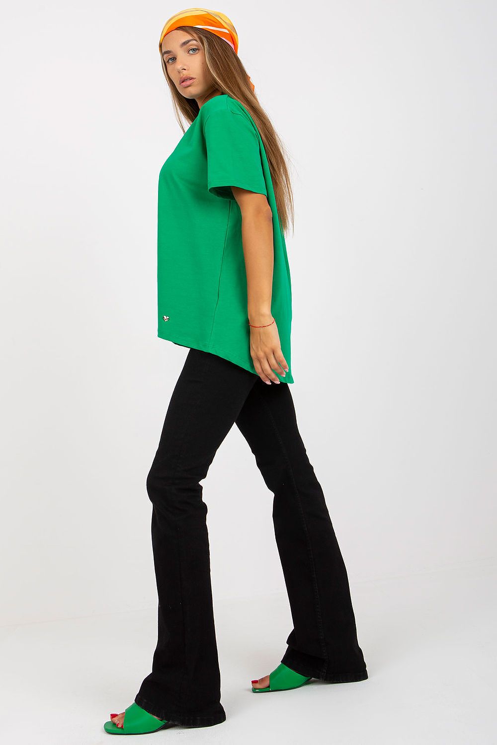 Side profile of a Luxury Women's BFG T-Shirt in vivid green, featuring an elongated back, elegantly modeled with flared black jeans for a fashionable look.