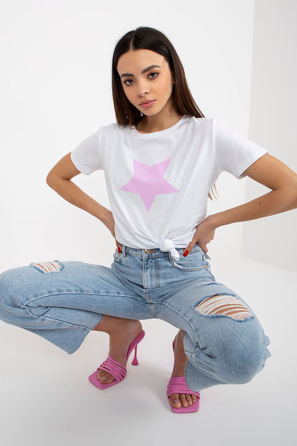 Fashionable woman sitting in a relaxed pose, wearing a luxurious women's BFG T-shirt with a pink star design, paired with trendy ripped denim jeans and stylish pink heels, embodying effortless elegance.