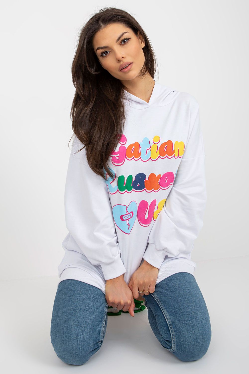 Elegant women's hooded sweatshirt in white featuring vibrant decorative text, designed by Fancy, showcased in a relaxed seated pose.