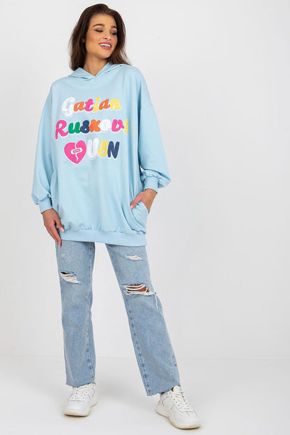 Chic women's hooded sweatshirt by Fancy in light blue, model smiling while displaying the decorative front lettering, perfect for casual style.