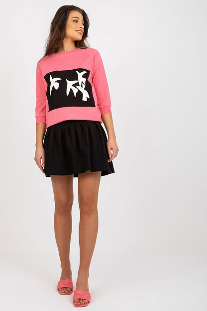 Stylish pink sweatshirt set from Fancy, displaying a round neckline and decorative print, elegantly paired with a black skirt for a luxurious look.
