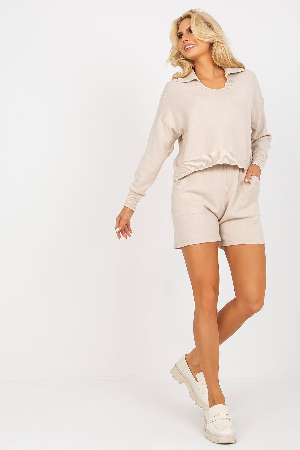 Charming model showcasing a luxury casual 2-piece set by EM, consisting of a looser cut sweater and short shorts, radiating effortless elegance.