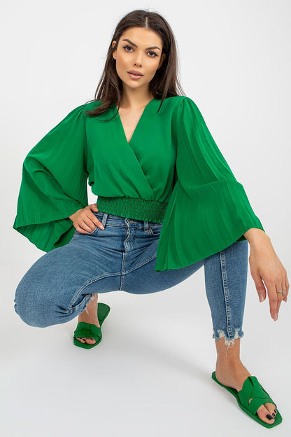 Stylish model sporting a green Italy Moda blouse with dramatic pleated sleeves, complemented by distressed jeans for a modern look.