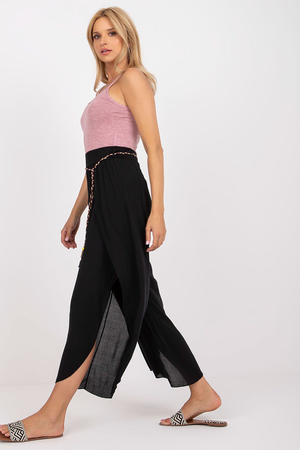 Side view of sophisticated high-waist trousers from Och Bella, adorned with a decorative waistband and flowing fabric, enhanced by the model's graceful silhouette.