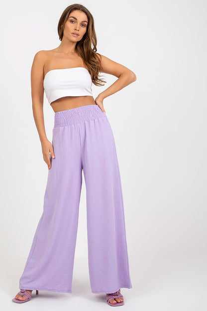Stylish woman showcasing luxury high-waisted trousers from Italy Moda, featuring a flowing wide-leg design in pastel lavender, paired with a chic white crop top.