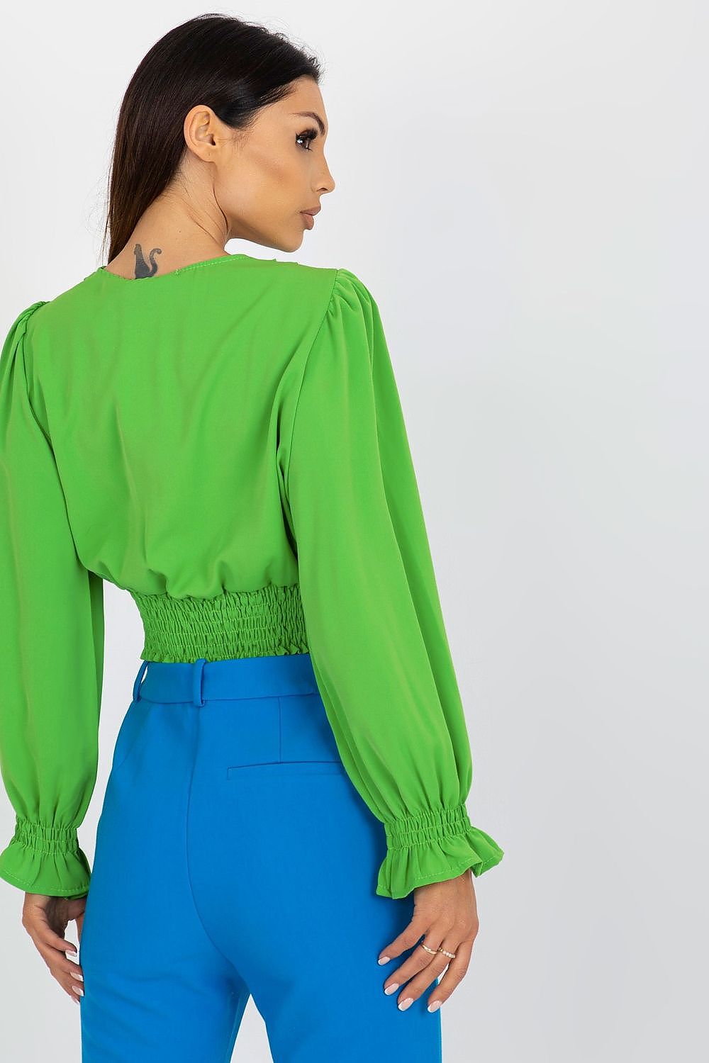 Back view of a model in a sophisticated green long sleeve blouse featuring an envelope neckline, styled with blue trousers, from Italy Moda.