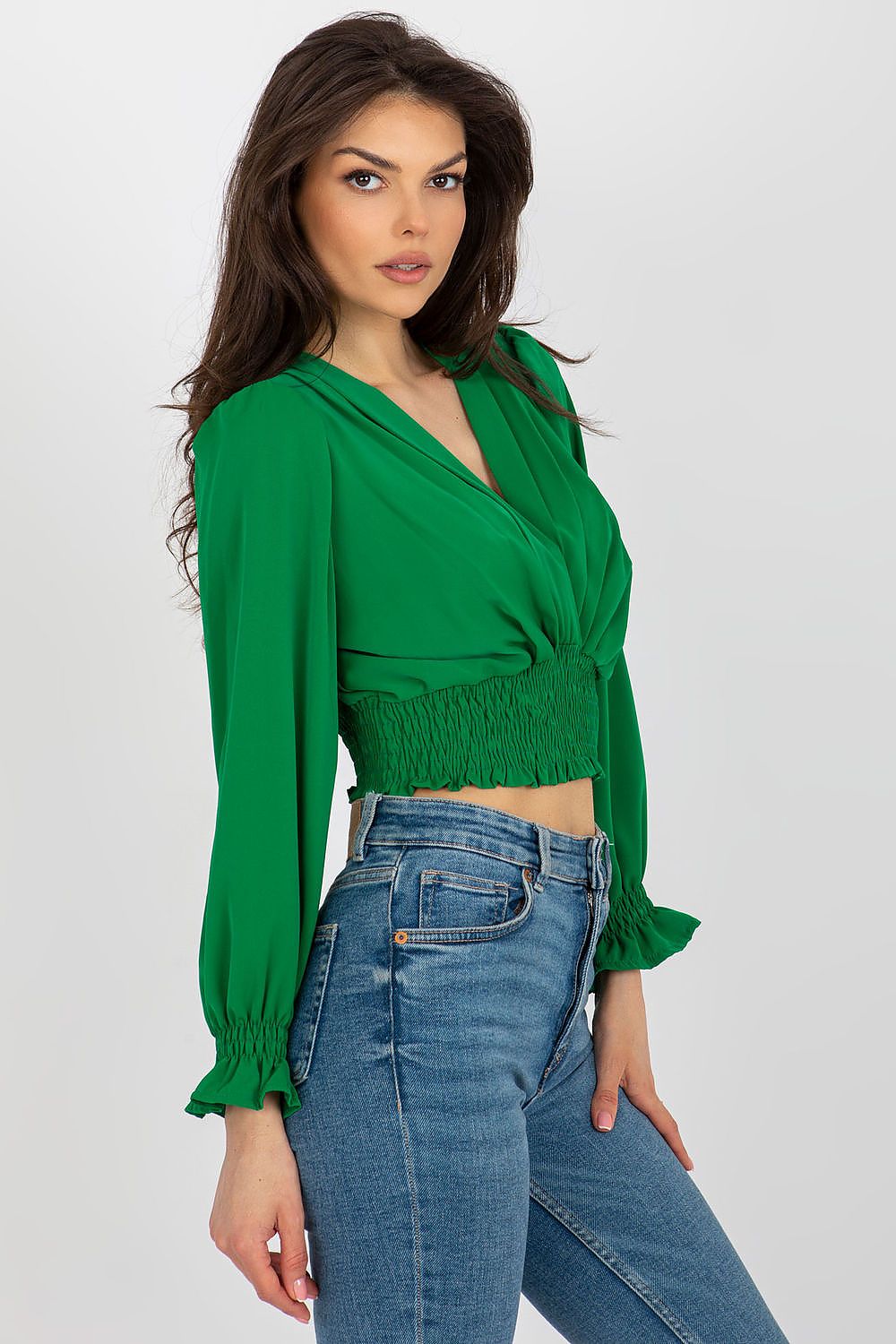 Beautiful model showcasing an elegant long sleeve green blouse with an envelope neckline and smocked waist from Italy Moda, paired with high-waisted denim jeans.