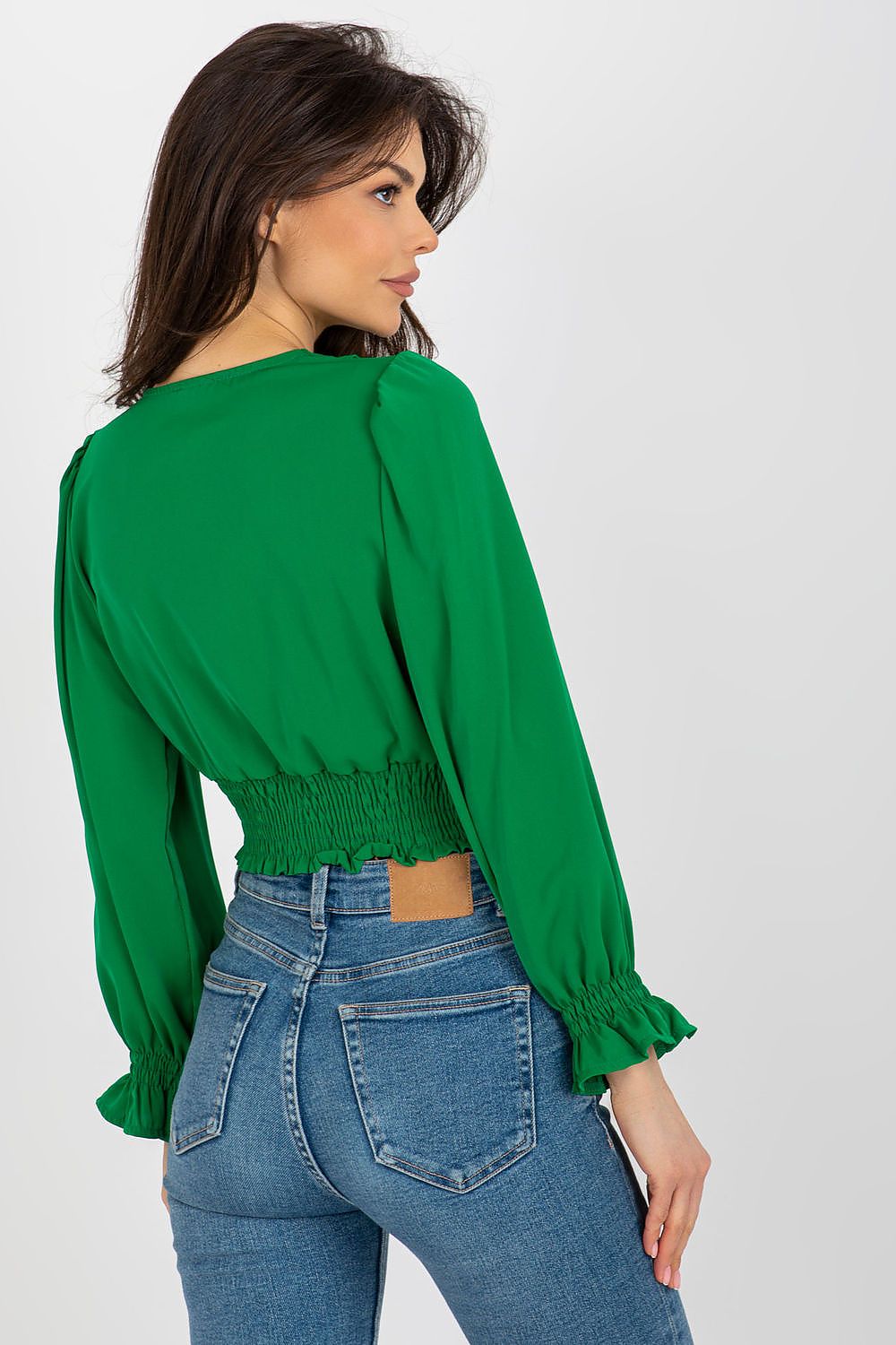 Charming rear view of a model wearing a sophisticated long sleeve green blouse with an envelope neckline and fitted smocked waist by Italy Moda, styled with blue denim jeans.