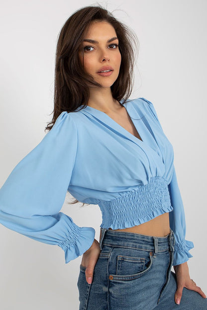 Stylish close-up of a model in a light blue blouse featuring an envelope neckline and smocked design at the waist from Italy Moda, perfectly matched with denim jeans.