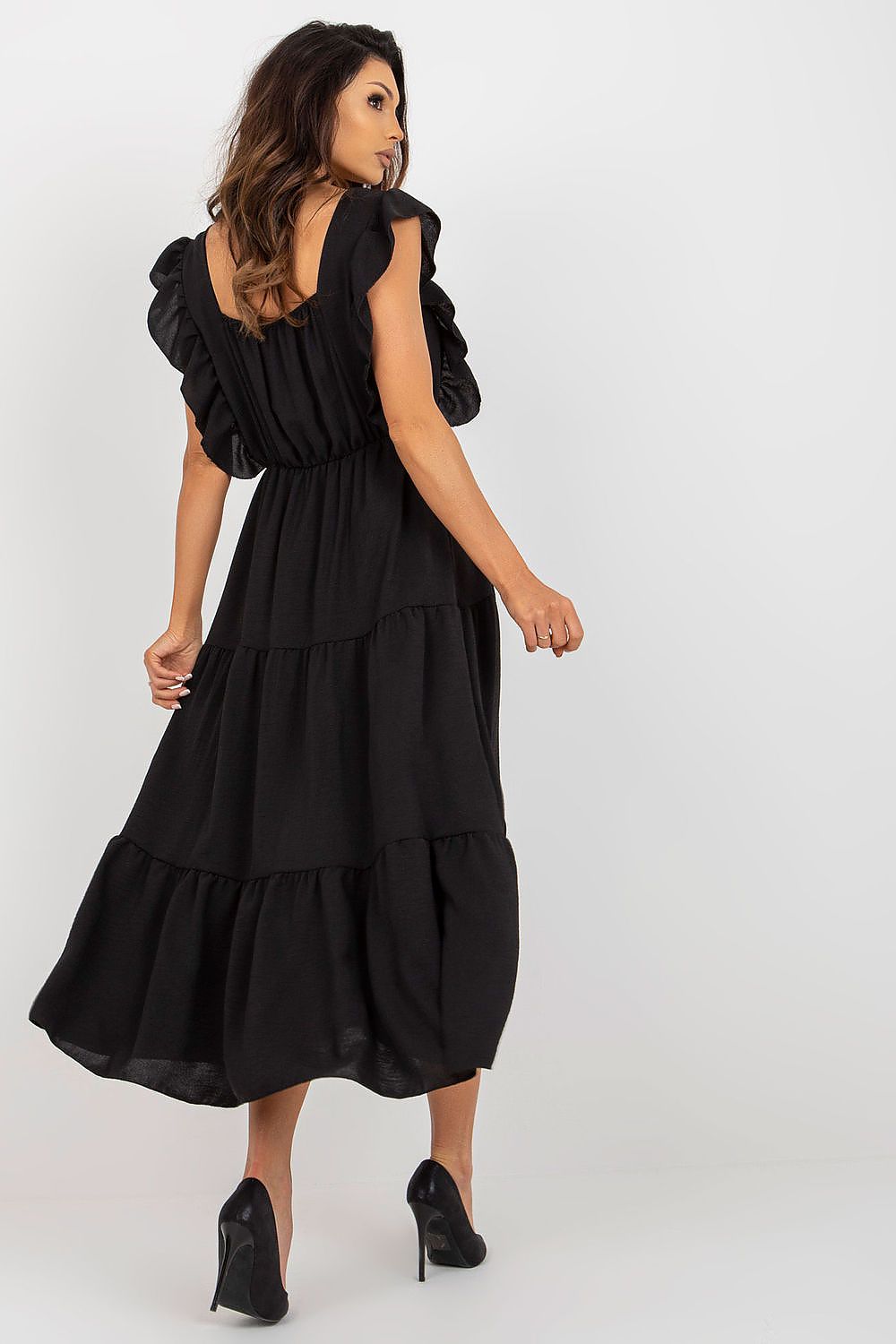 Back view of a sophisticated black summer dress with ruffled detailing and tiered hemline by Italy Moda, elegantly paired with high-heeled shoes.