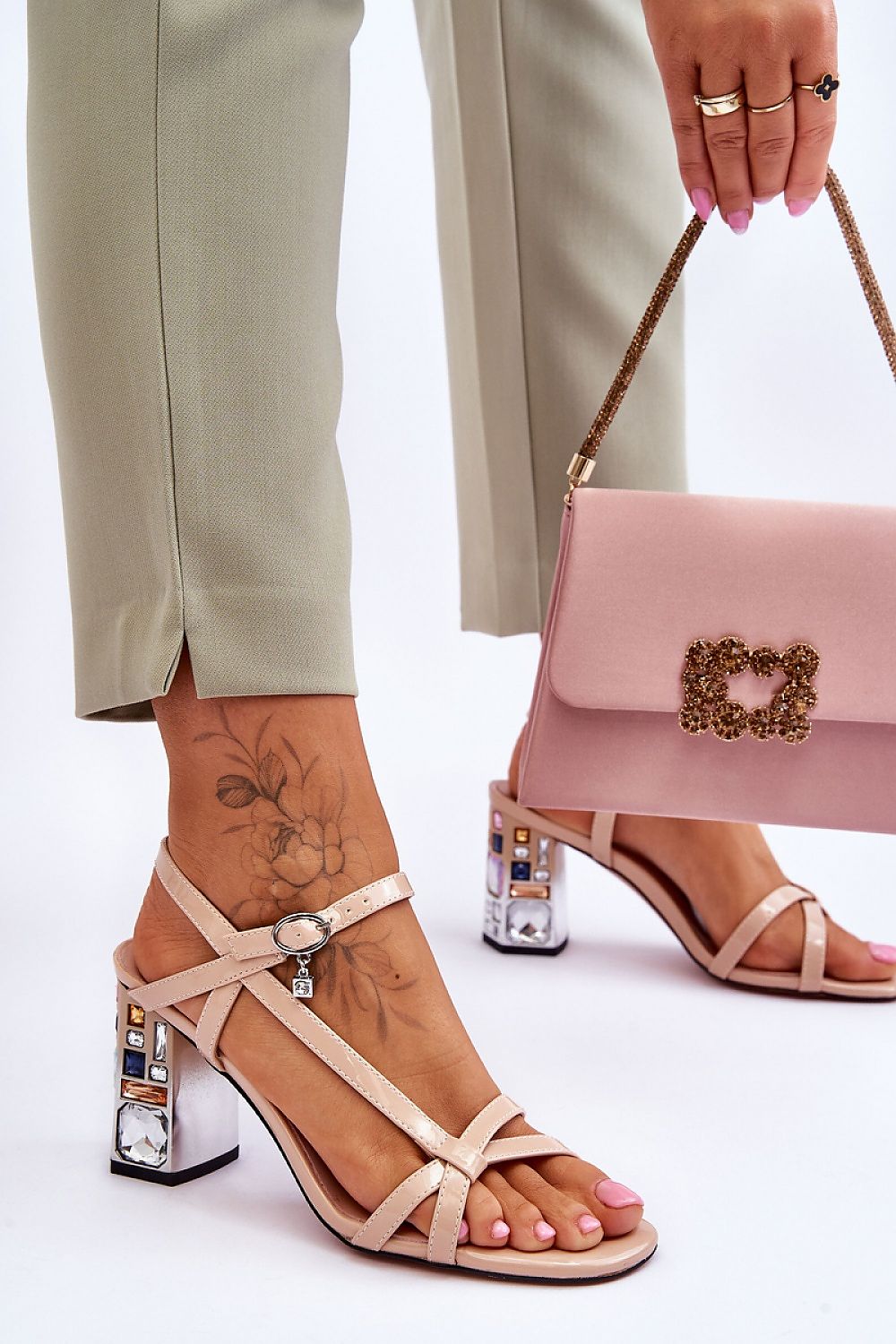 Sleek nude sandals with intricate detailing by Step in Style, embellished with embellishments, worn alongside elegant trousers and a chic pink handbag.
