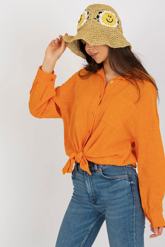 Close-up of a fashionable woman wearing the Och Bella cotton long sleeve shirt in orange, with a knotted front detail, accessorised by a playful bucket hat, embodying a luxe casual look.