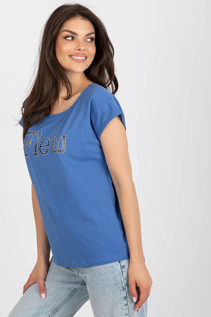 Trendy blue casual t-shirt for women by Fancy, featuring an elegant cut-out inscription 'Flew'. The model showcases a bright smile while highlighting the versatile styling options.