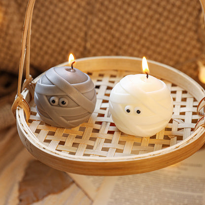 Elegant Halloween Scented Candle Set showcasing two adorable mummy-shaped spherical candles, one white and one grey, glowing warmly in a rustic basket.