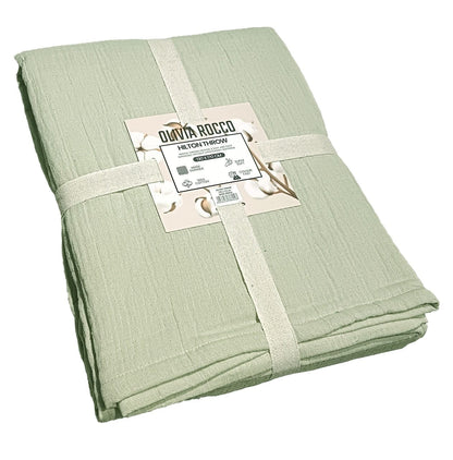 Full view of the Hilton Reversible Throw Blanket draped over a sofa, highlighting its elegant two-tone design in sage green and natural, epitomising comfort and sophistication.