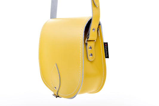 Close-up of the adjustable crossbody strap of the pastel daffodil yellow leather saddle bag, highlighting luxury materials and timeless aesthetic.
