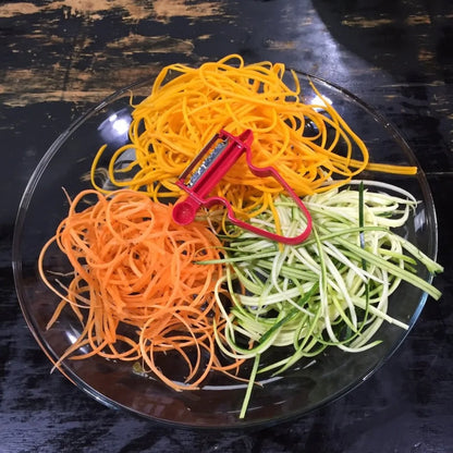 Artful display of spiralized vegetables, featuring a red peeler, showcasing the Magic Trio Peeler's ability to create gourmet garnishes and elegant presentations.