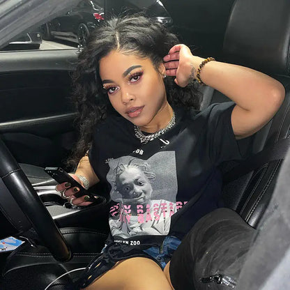 Woman in a stylish Women's ODB Graphic Print Tassel Tee, showcasing urban chic fashion while seated in a car, featuring curly hair and striking makeup.