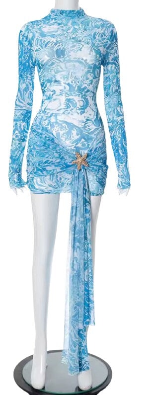 Santorini Dress displayed elegantly on a hanger, emphasizing the luxury shear print and the beautiful starfish brooch detail.