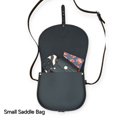 Elegant black leather saddle bag with oversized front flap, featuring contrasting stitching and customizable engraving options, perfect for stylish everyday use.